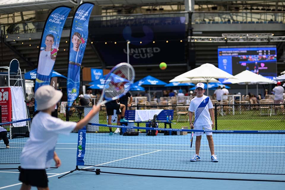 Image of 2 kids hitting a tennis ball on a blue court